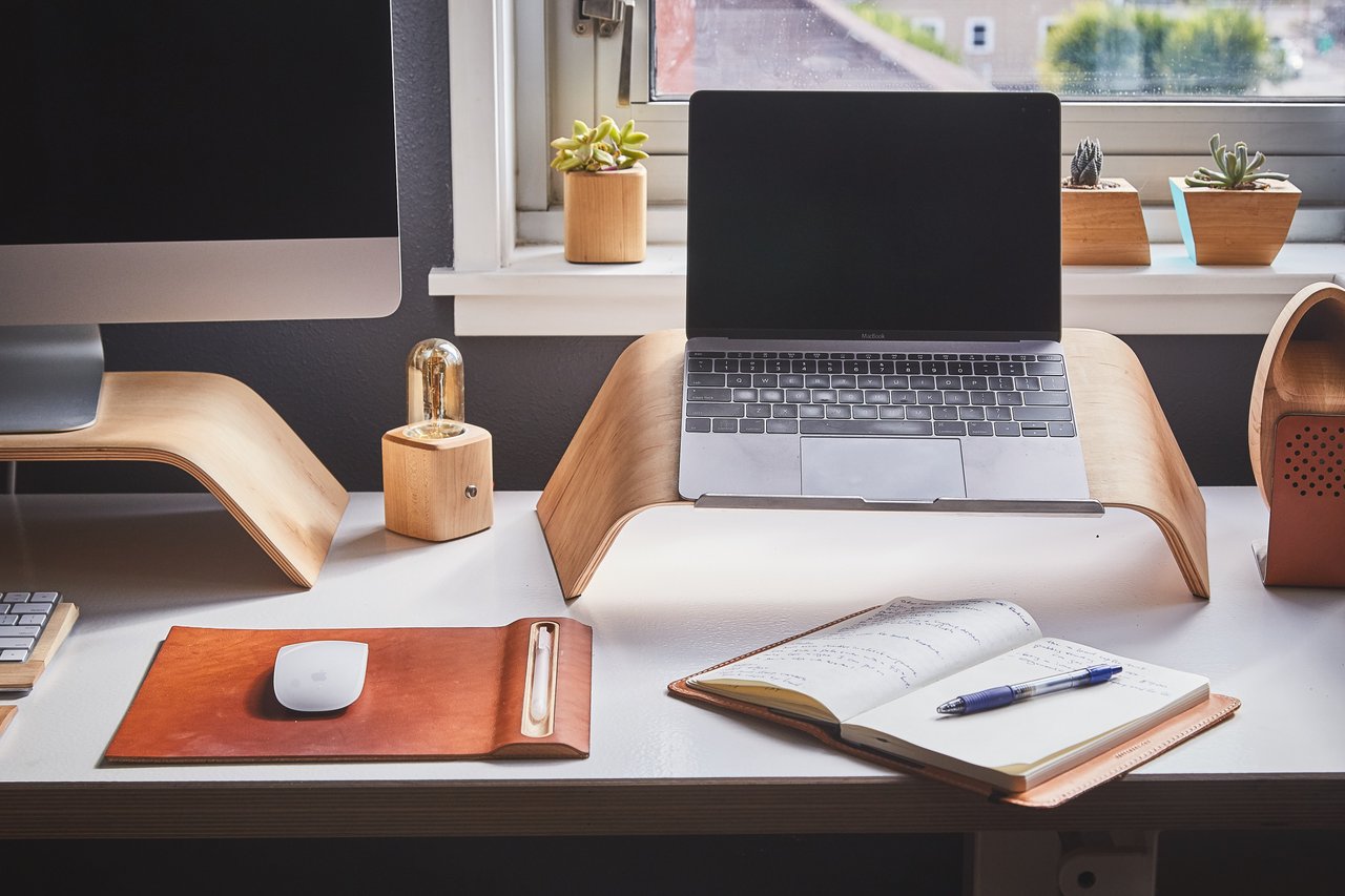 Home-office desk with a laptop, monitor, open notebook, and potted succulents.
