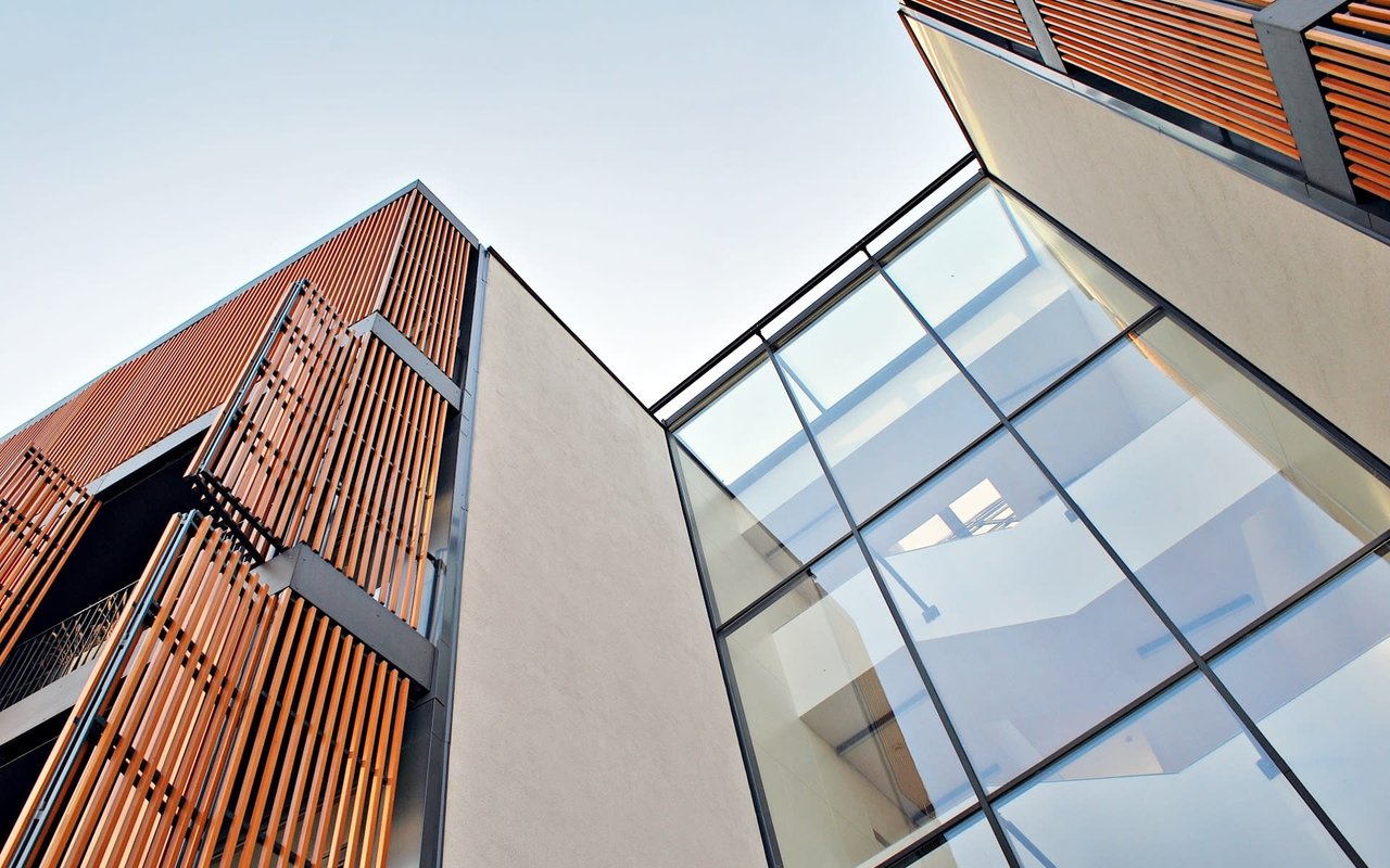 A tall, modern building with a glass facade and a blue sky in the background. The building is casting a warm glow.