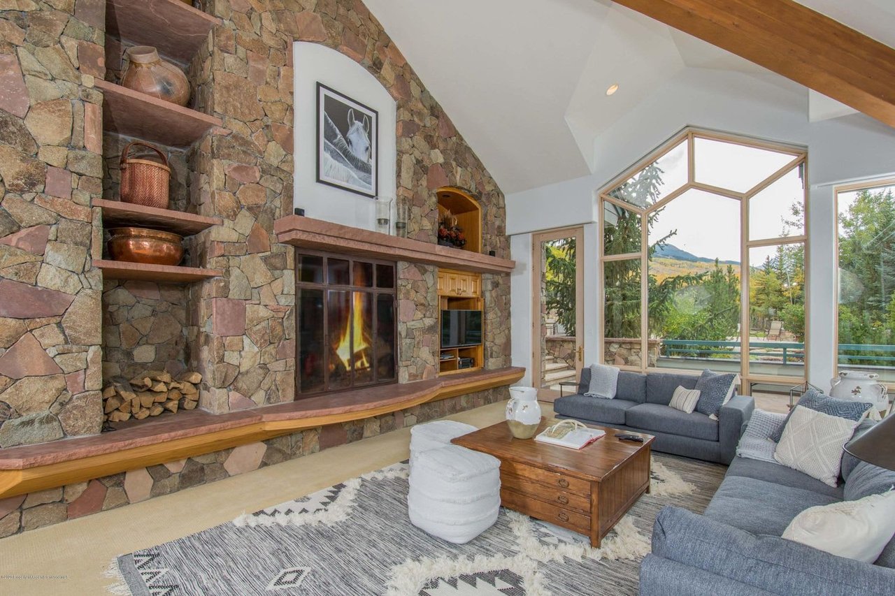 Living room with a stone fireplace, vaulted ceiling, and large windows overlooking the mountains.