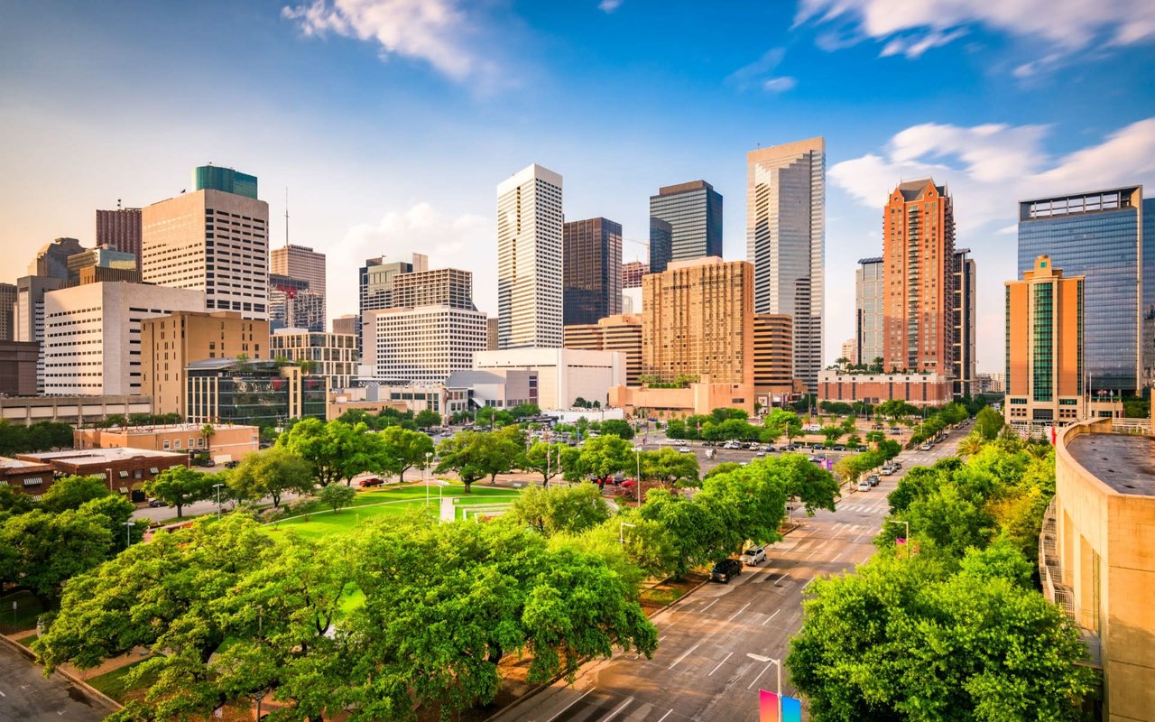 View of the Houston skyline with diverse architectural styles among skyscrapers, surrounded by lush greenery.