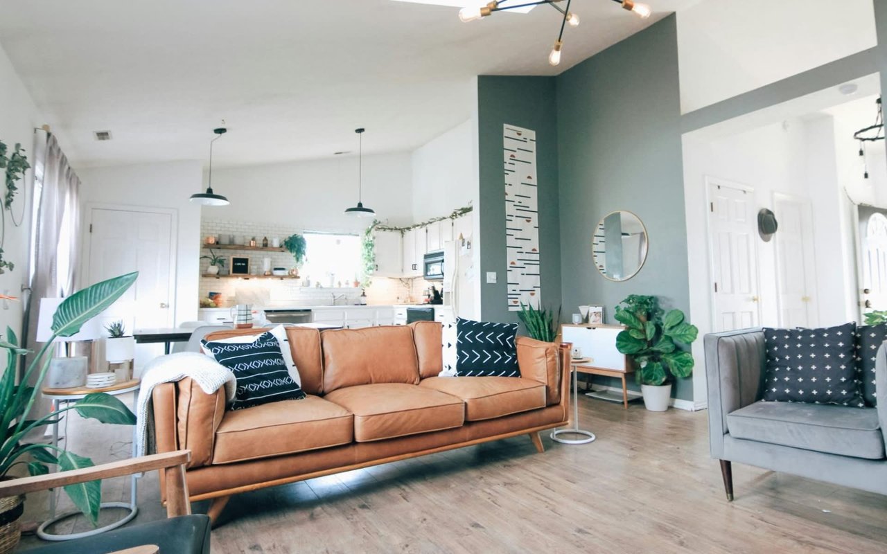 Scandinavian-inspired living room with tan leather sofa, gray accent chair, and open kitchen with pendant lights.