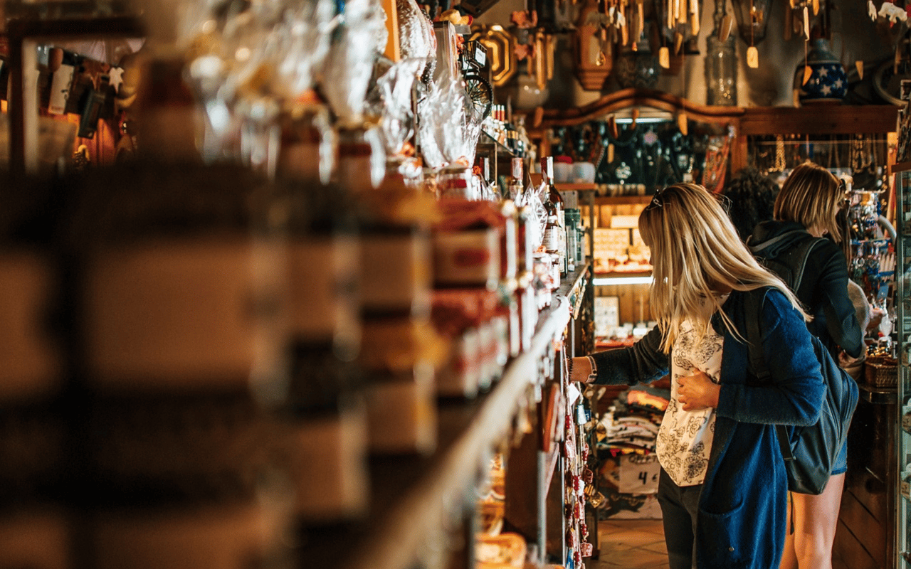 Two women browse shelves of souvenirs and gifts in a warmly lit shop.
