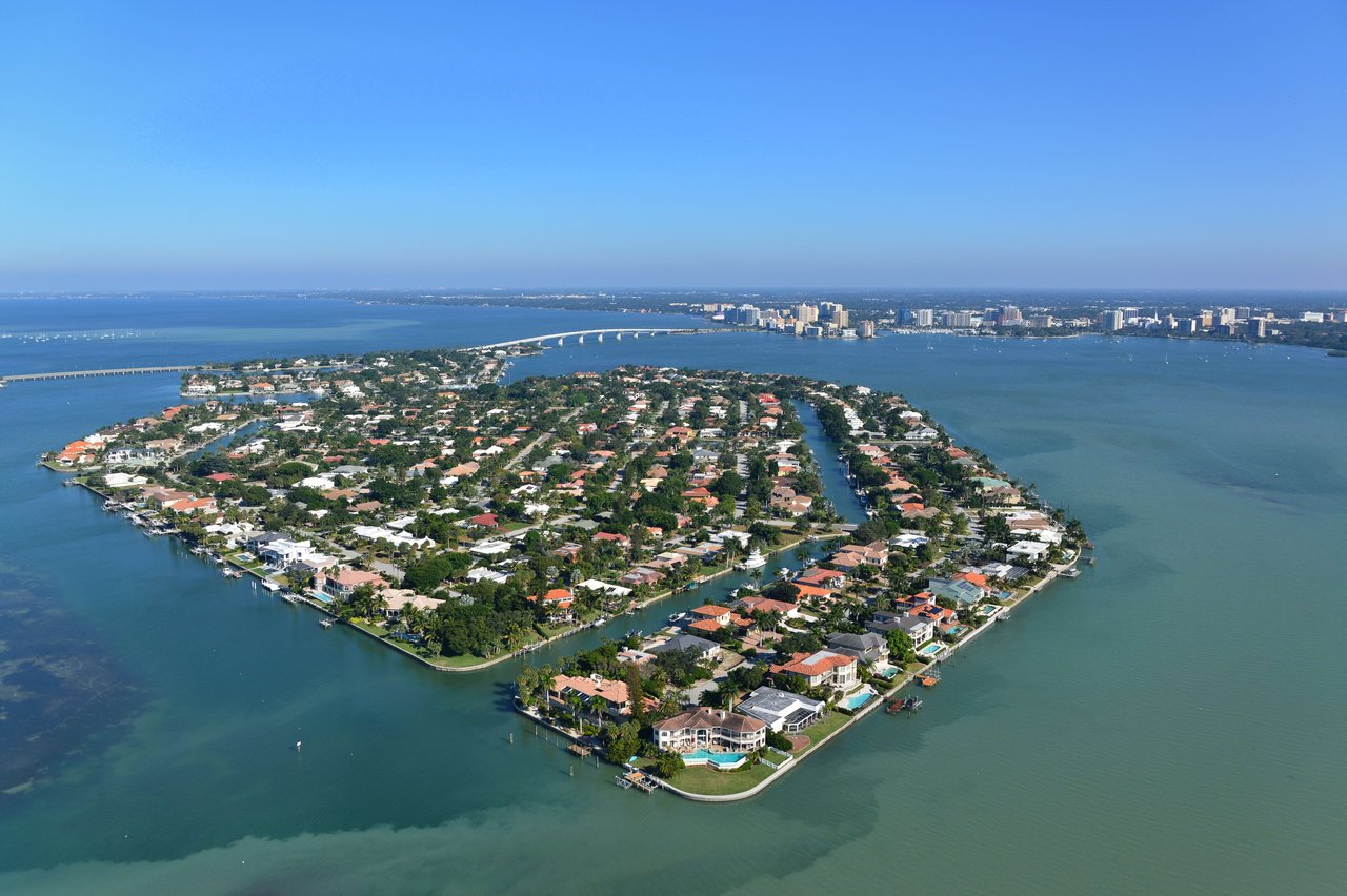 Aerial view of a lush island with upscale homes, canals, and stunning bay views.