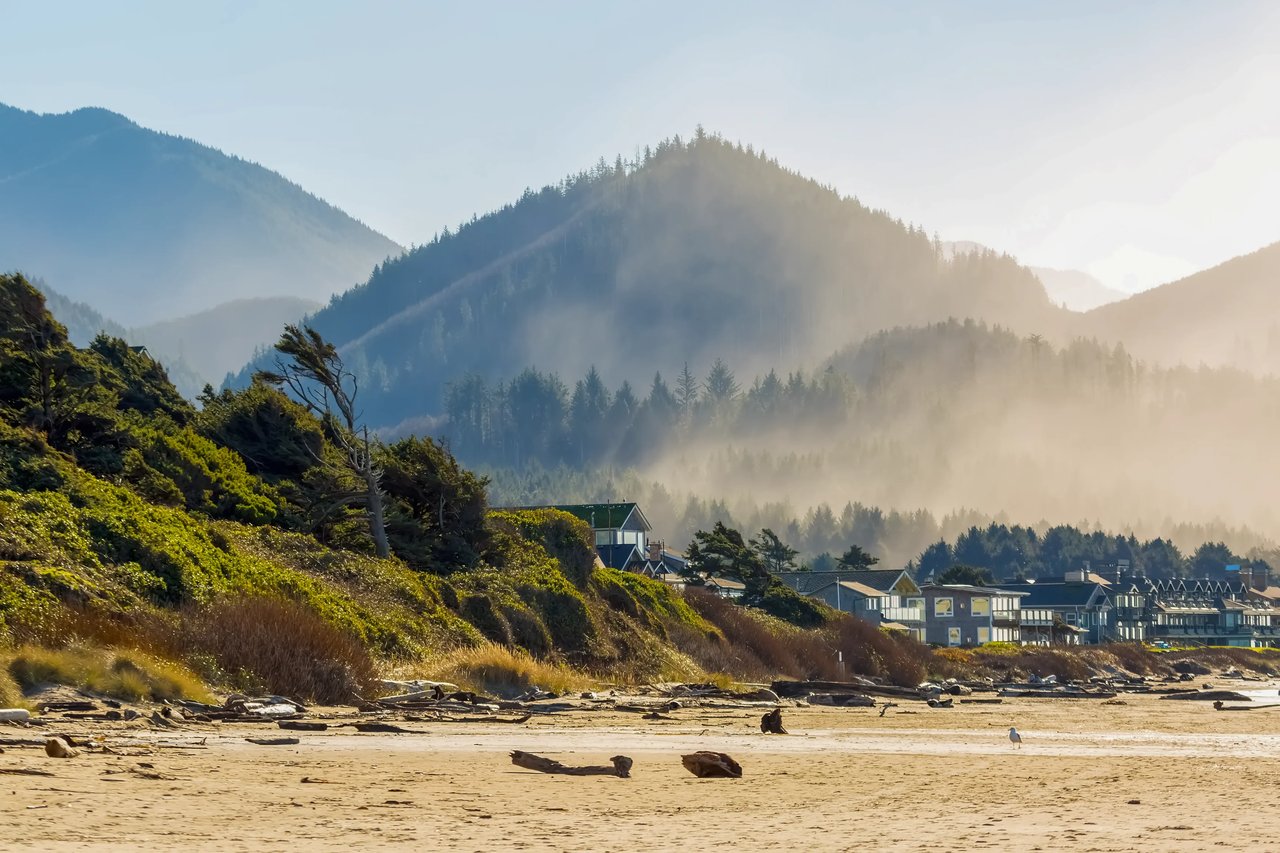 Homes and hotels on the beach in Cannon Beach with misty tree covered hills behind them