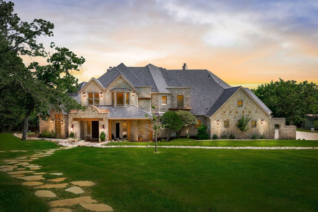 A large stone house with a spacious lawn is bathed in the warm glow of sunset with a peaceful and serene mood.