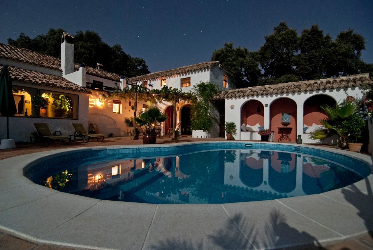 Nighttime view of a Spanish-style courtyard with a round pool, arched walls, and ambient lighting.