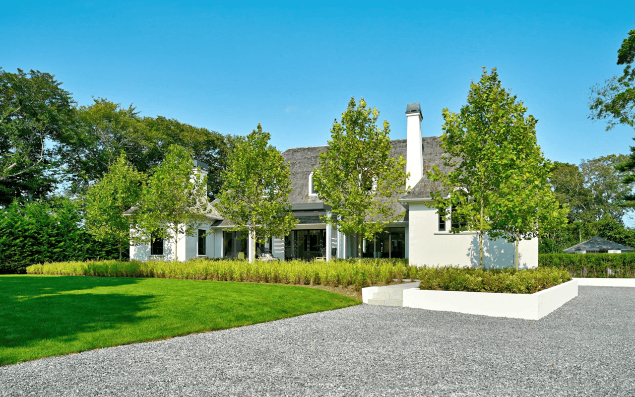 A luxurious, contemporary home with a flat roof and large glass windows is set amidst a vibrant green landscape.
