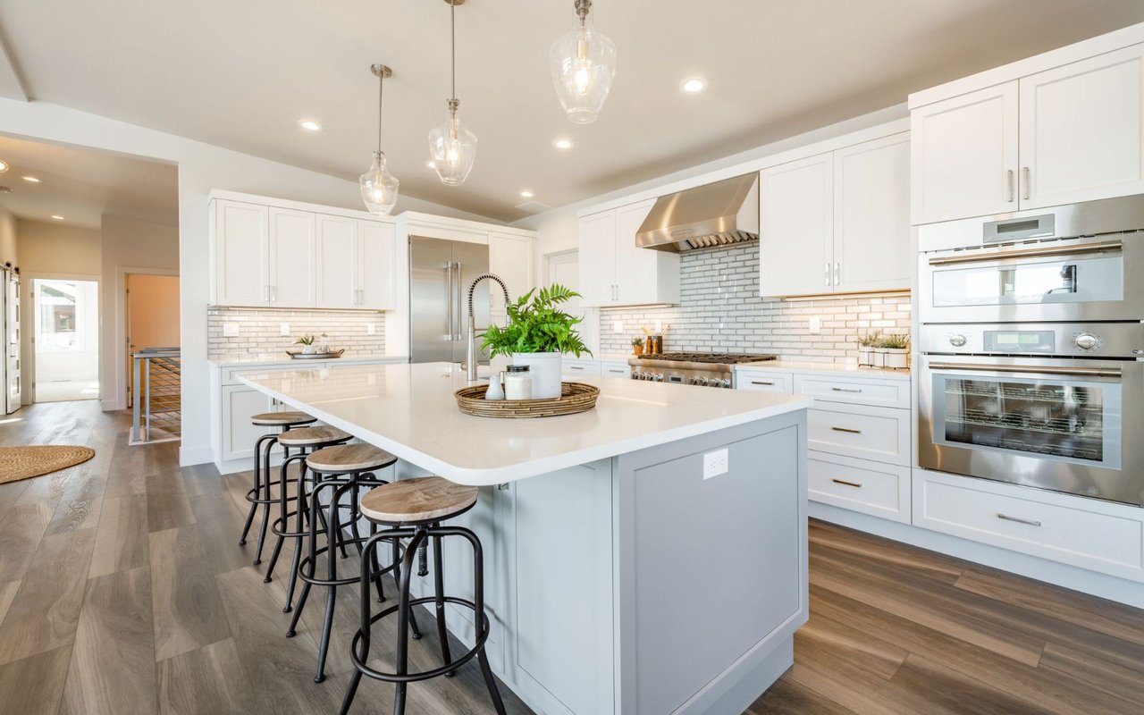 A modern kitchen with a large island in the center, stainless steel appliances, bar stools, and hanging pendant lights.