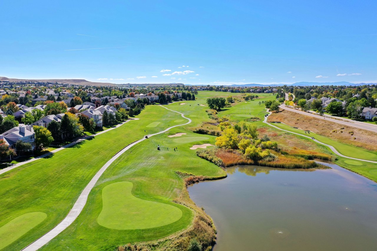 Aerial view of a golf course with a lake and houses in the background