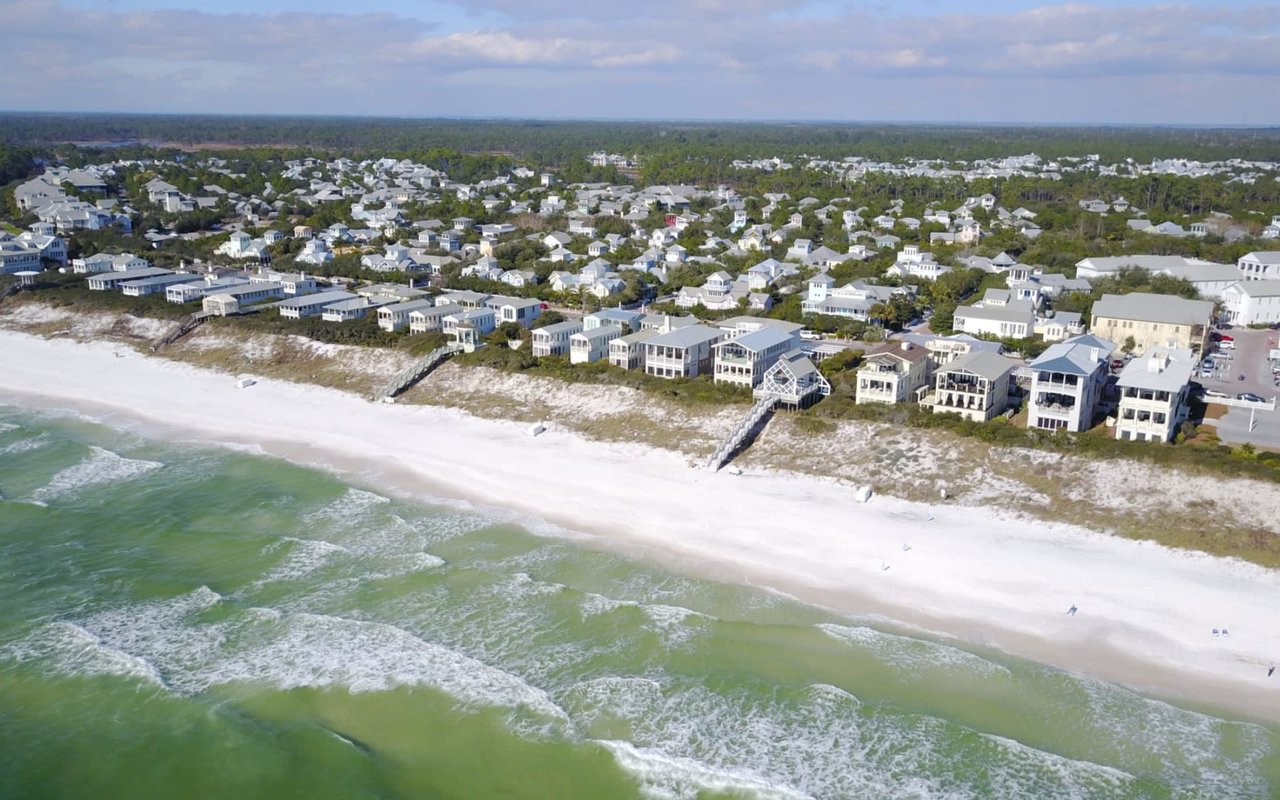 An aerial view of a coastal town with white sand beaches, turquoise water, and colorful houses.