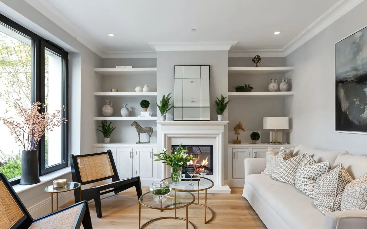 A living room with a fireplace, a white sofa, and built-in shelves decorated with vases, plants, and artwork.