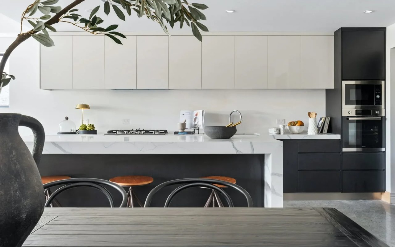 A kitchen with white upper cabinets, black lower cabinets, a white marble countertop, a dining table, and black chair.