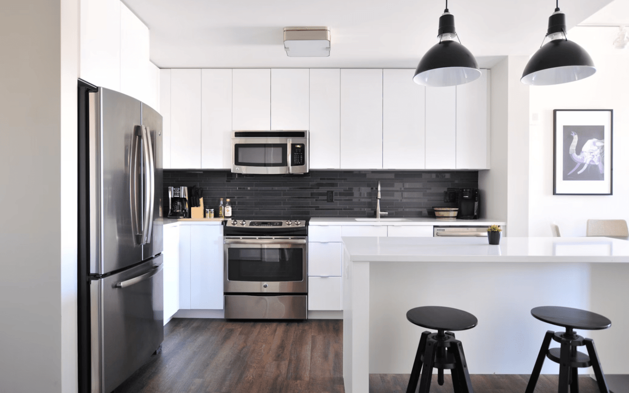 A sleek and modern kitchen with white upper and lower cabinets and a dark grey subway tile backsplash