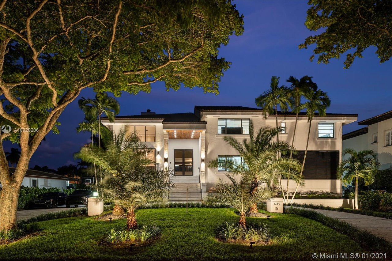 The house features multiple windows and a prominent dark front door, with warm lights glowing from its exterior.