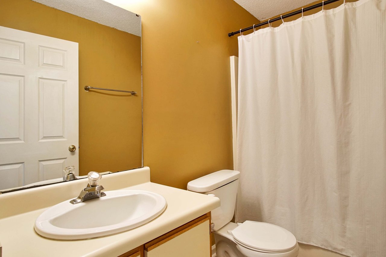 Photo of guest bathroom featuring yellow walls, a vanity light fixture, a large mirror, a vanity, the toilet, and a bathtub  at 2709 Oak Park Court, Tallahassee, Florida 32308