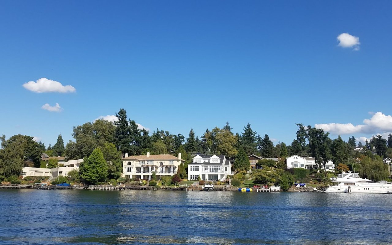 A group of houses with white walls and green trees nestled on a lakeside overlooking a calm blue lake.