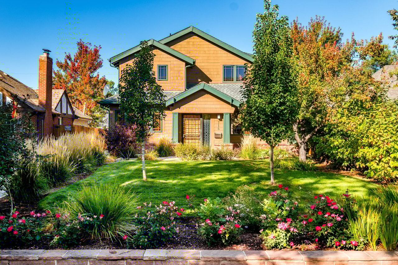 Two-story house with dormer windows, slate roof, picket fence, and green front yard.