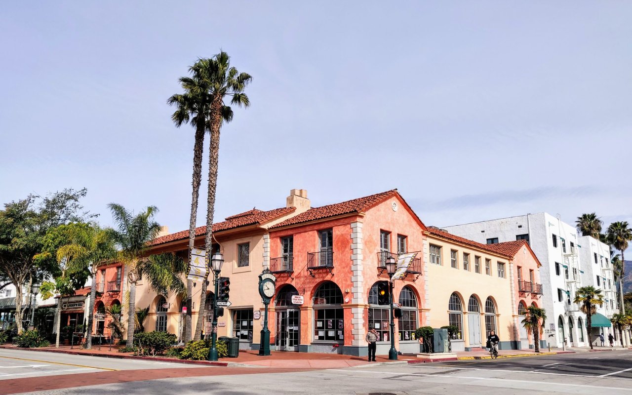 A historic building with a terracotta roof and arched windows stands on a corner in downtown Santa Barbara.