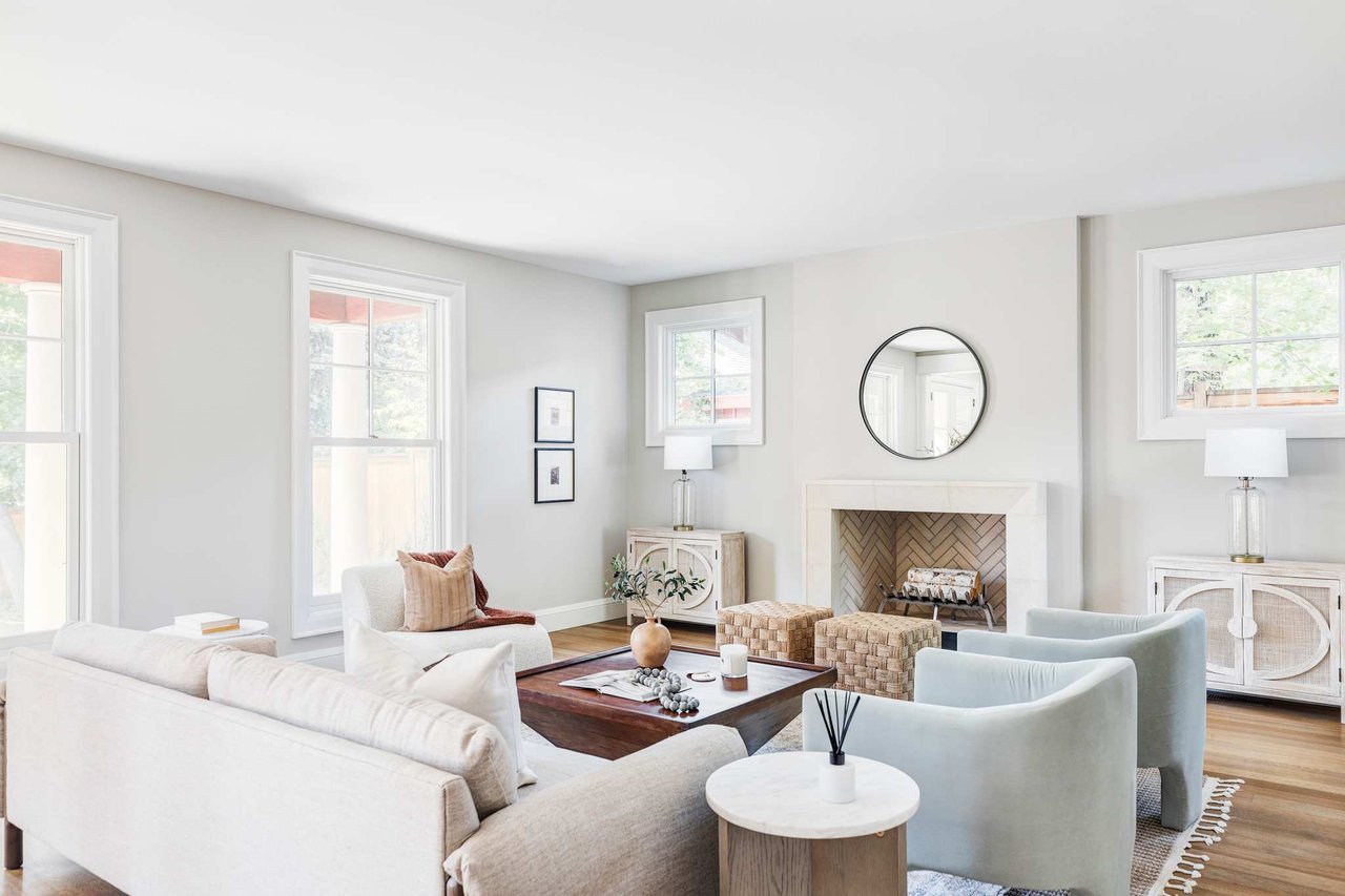 White living room with herringbone fireplace, cream sofas, blue accent chairs, and natural wood details.