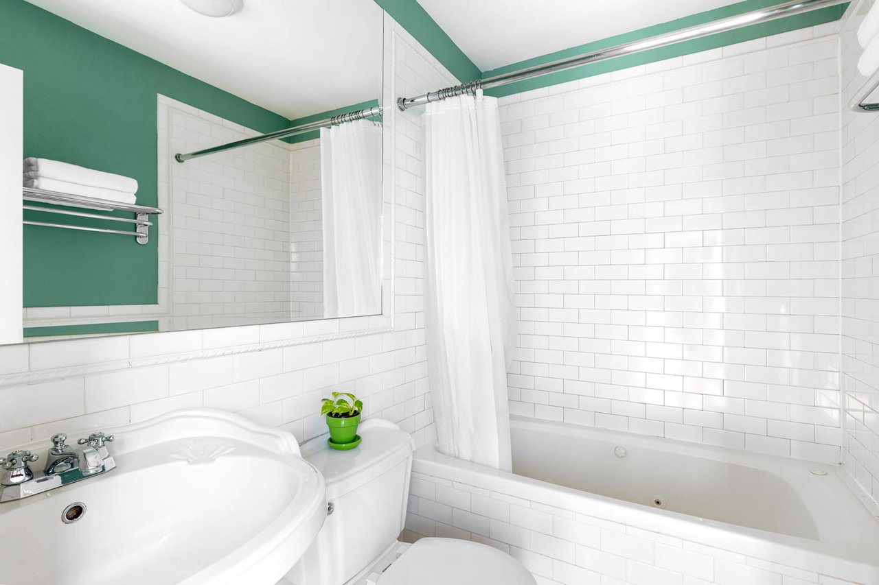 Bathroom with a white tiled tub and shower, large mirror, and green walls.