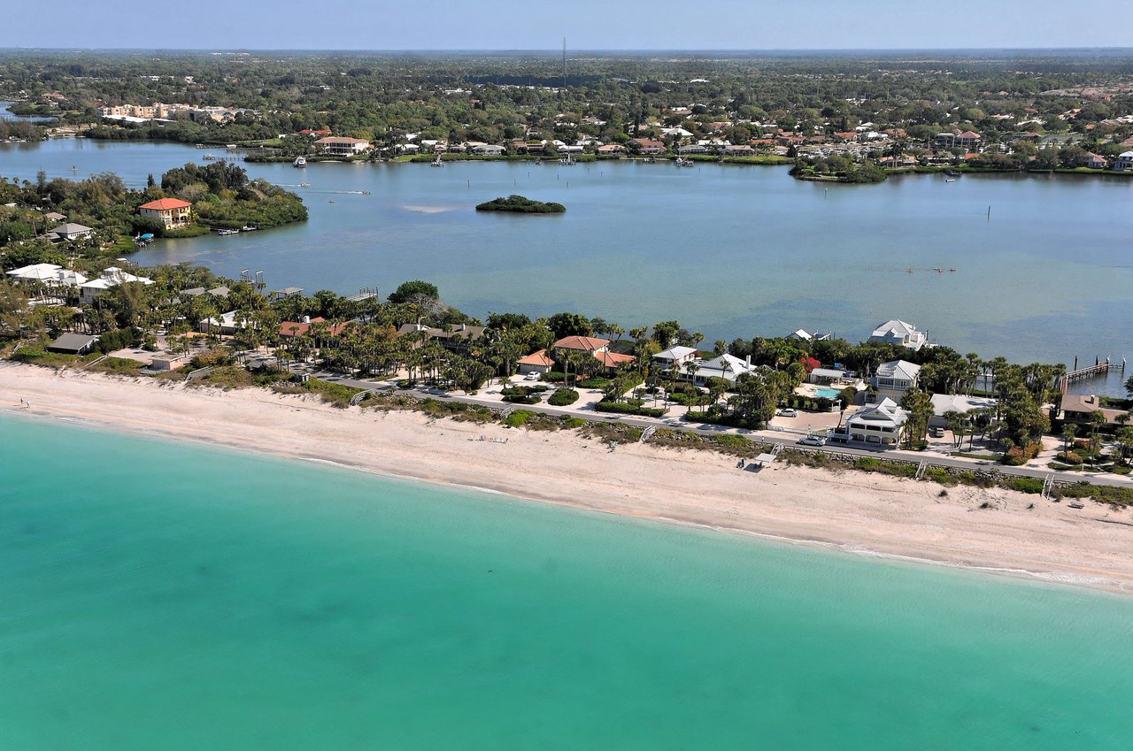 Aerial view of white sandy beach, turquoise water, lush vegetation, and upscale homes lining the coast.