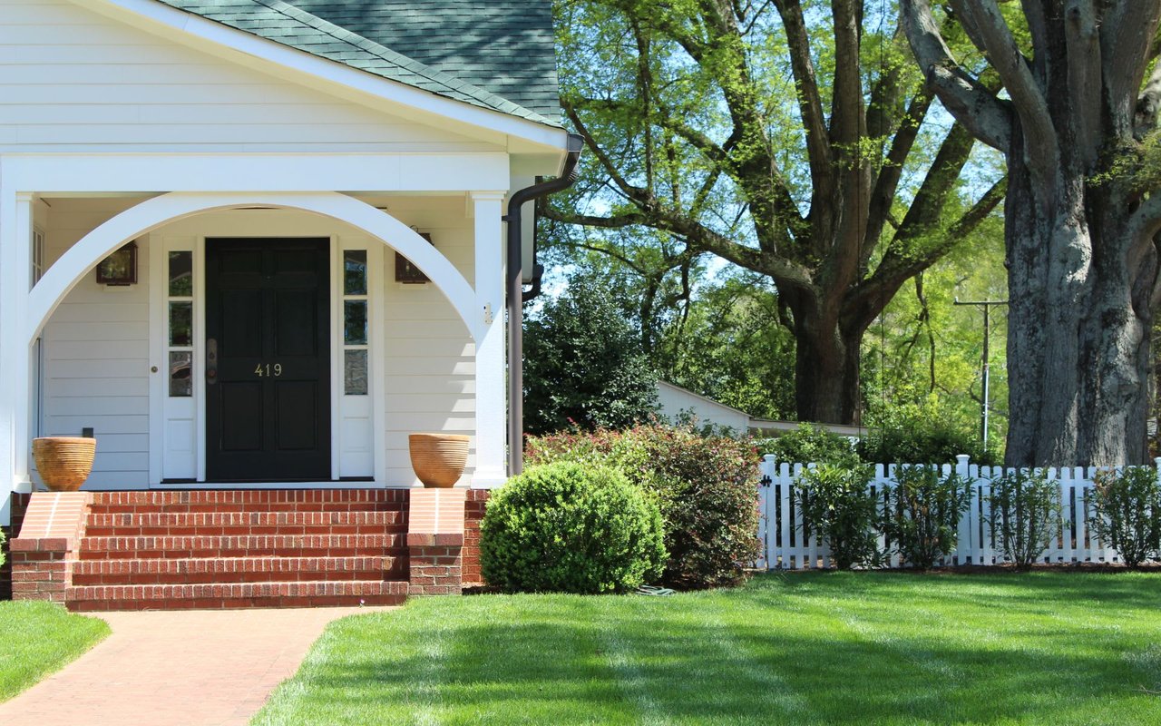 Classic white single-family house with a black door and brick steps, mailbox, lamppost, and horizontal wooden panel siding.