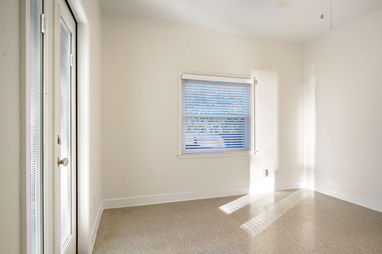 An interior shot of the second bedroom. The room is bright and spacious with large windows, a door leading outside, and a neutral color palette.