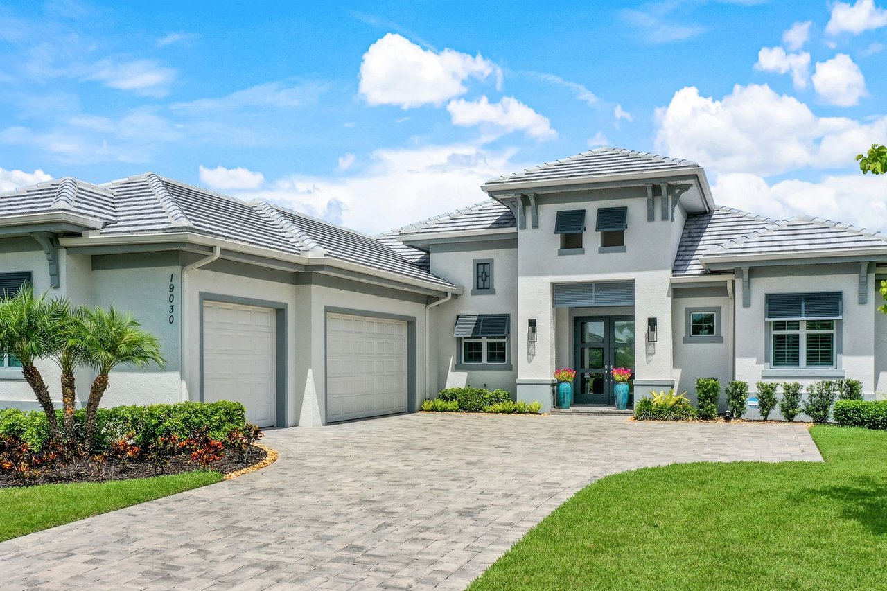 A luxurious, modern white house with a grey tiled roof and a large paver driveway