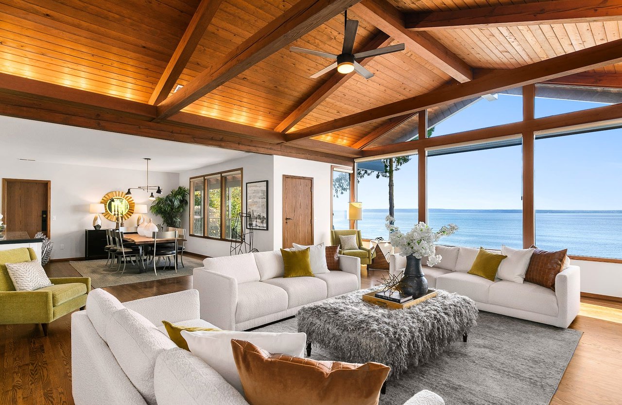 A living room with a wooden ceiling and a large window showcasing a view of the ocean.