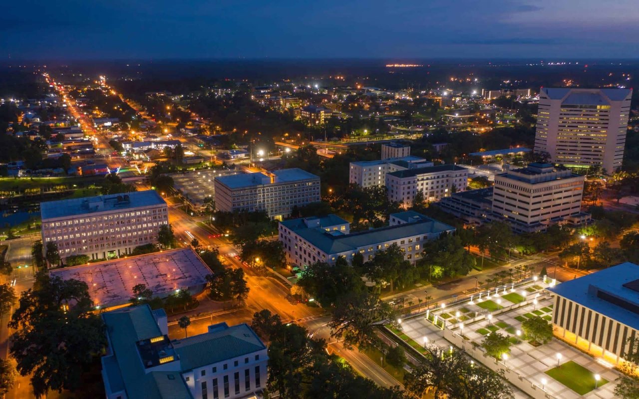 An aerial view of a city at night, with buildings and streets illuminated. 