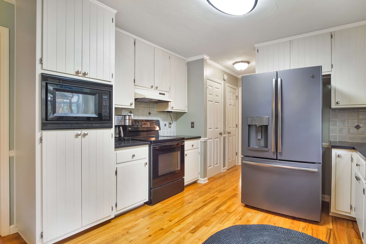 This kitchen also has white cabinets, stainless steel appliances, and wooden flooring, creating a cohesive design.