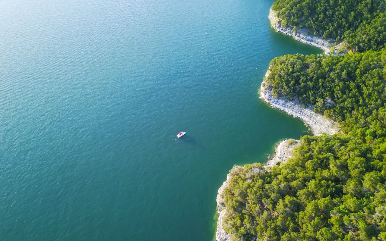 An aerial view of a boat sailing serenely in the middle of  Lake Travis, surrounded by breathtaking natural beauty.