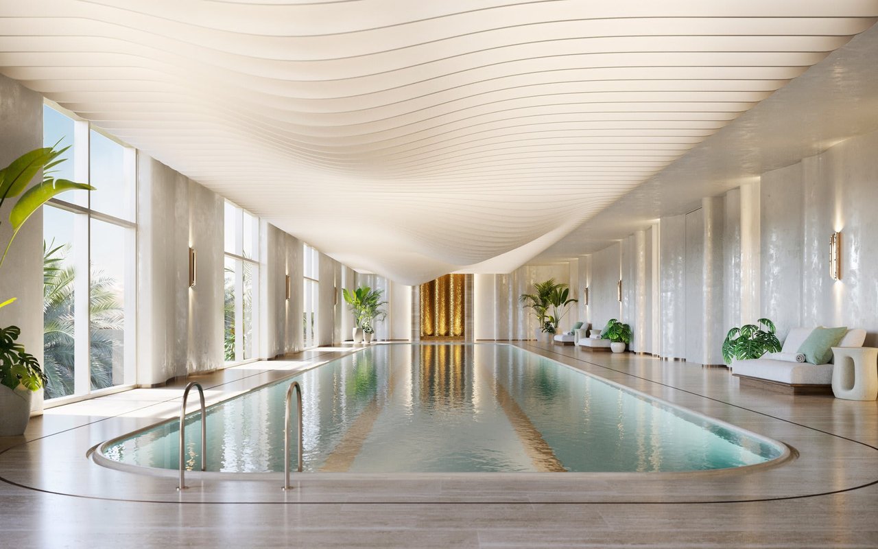 Indoor swimming pool beneath a sculptural ceiling, with marble walls and floor-to-ceiling windows.
