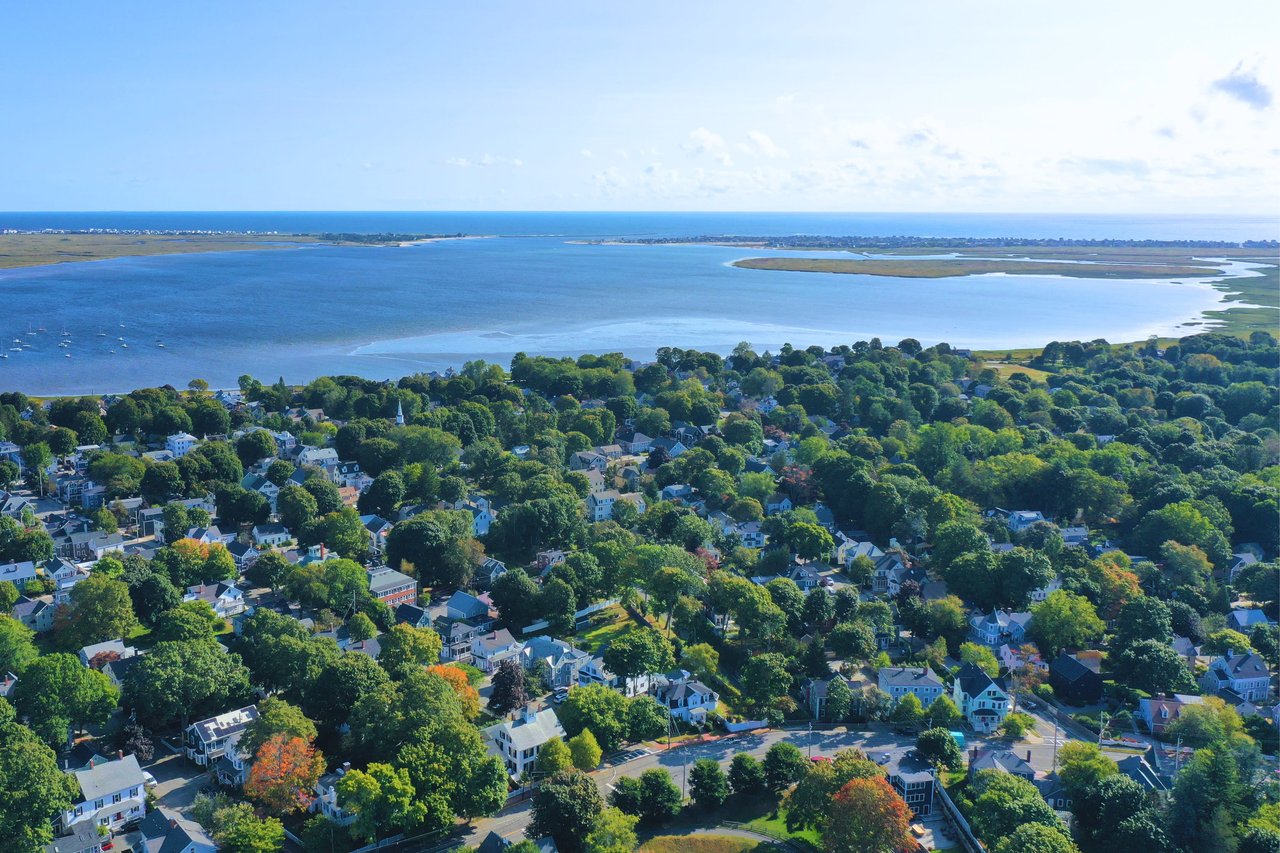  An aerial view reveals a vibrant coastal town nestled beside a large body of water, likely an ocean, with a long, narrow spit of land in the distance. 