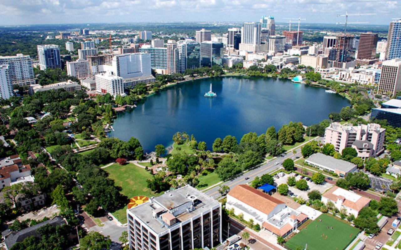 An aerial view of a lake in the middle of a city, surrounded by tall skyscrapers, parks, and green spaces.