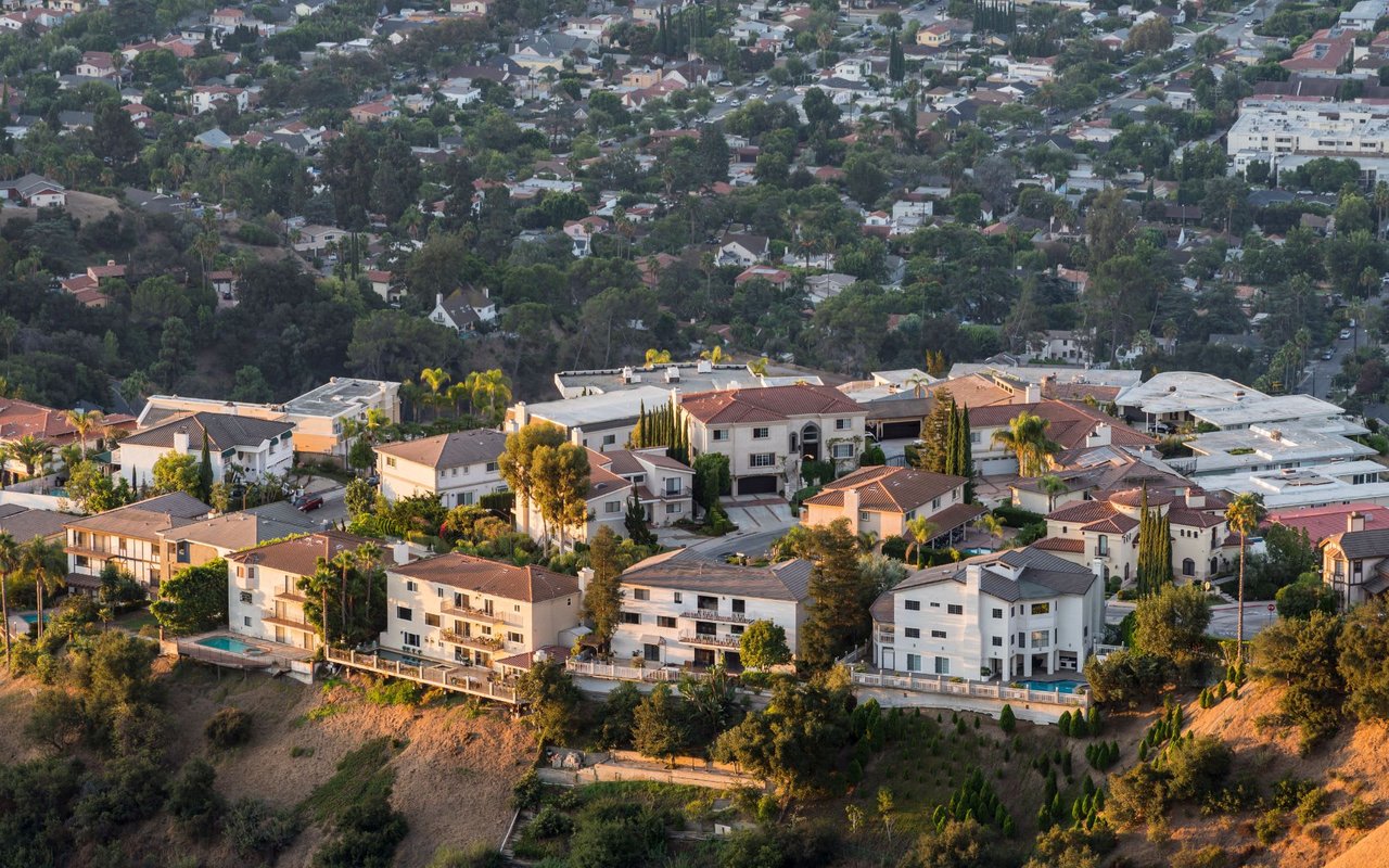 Aerial view of Mediterranean-style houses with red roofs and palm trees on a hillside in Los Angeles, under a clear blue sky.