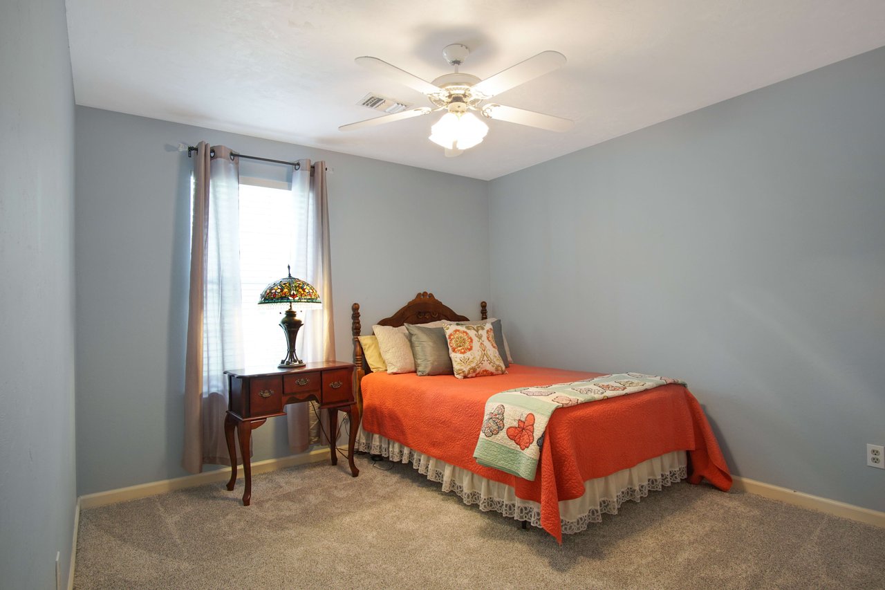 An interior shot of a bedroom with blue walls and a red bedspread. The room has a closet with white doors and carpeted flooring.
