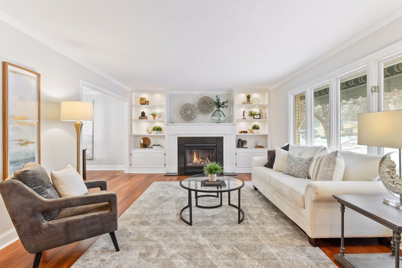 A staged living room with a white couch, gray chair, fireplace, and coffee table with a glass top.