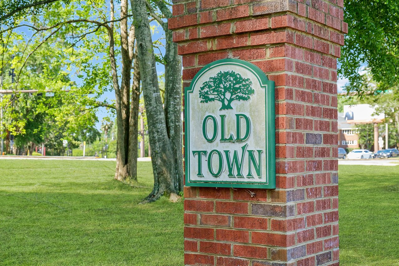 A ground-level view of a brick sign for "Old Town," indicating the neighborhood entrance, with trees and greenery around it.