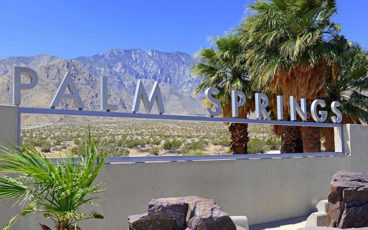 Palm Springs entrance sign with palm trees and desert mountains behind it.