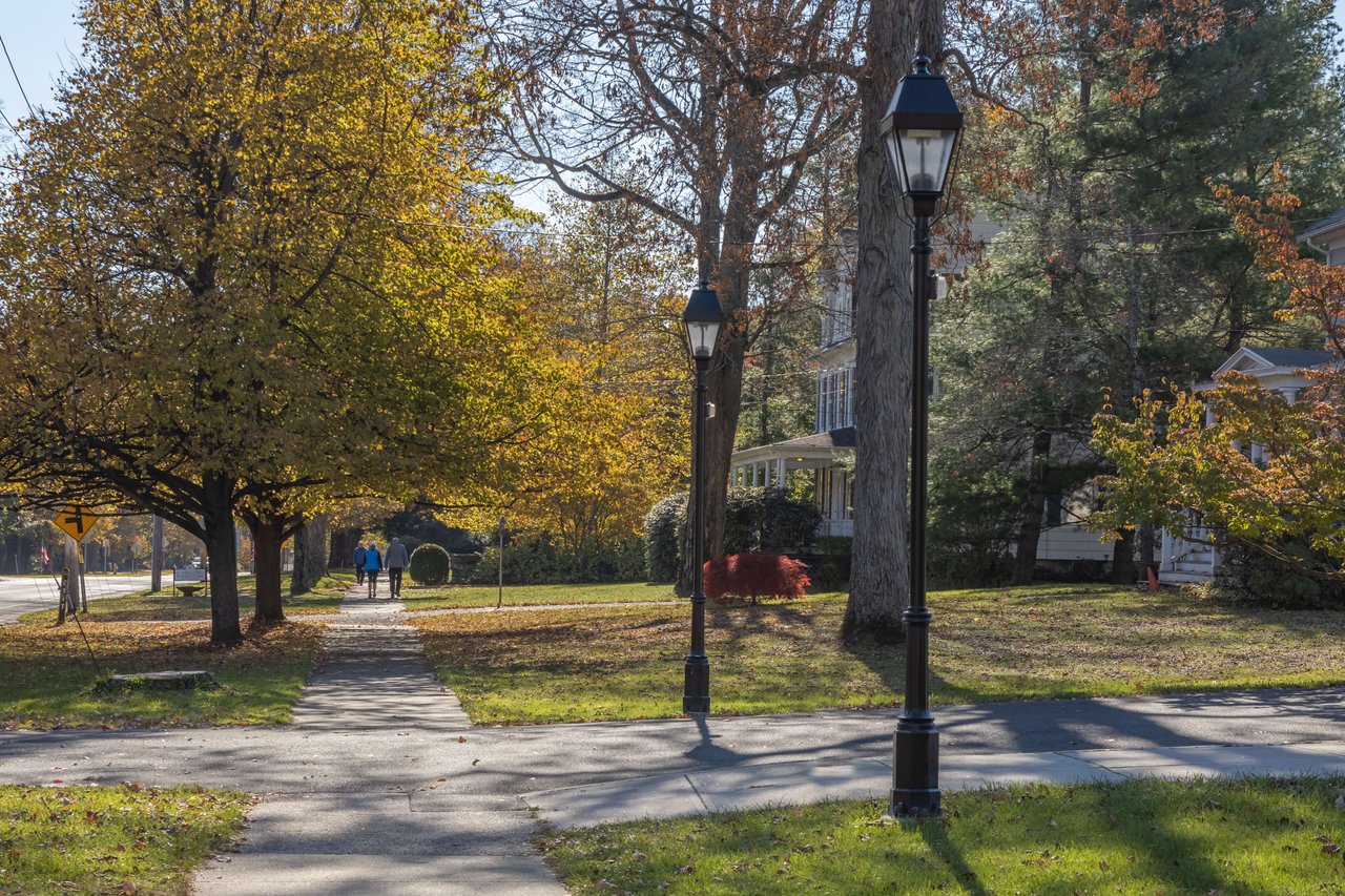 A couple walking down a tree-lined sidewalk with trees covered in autumn leaves.