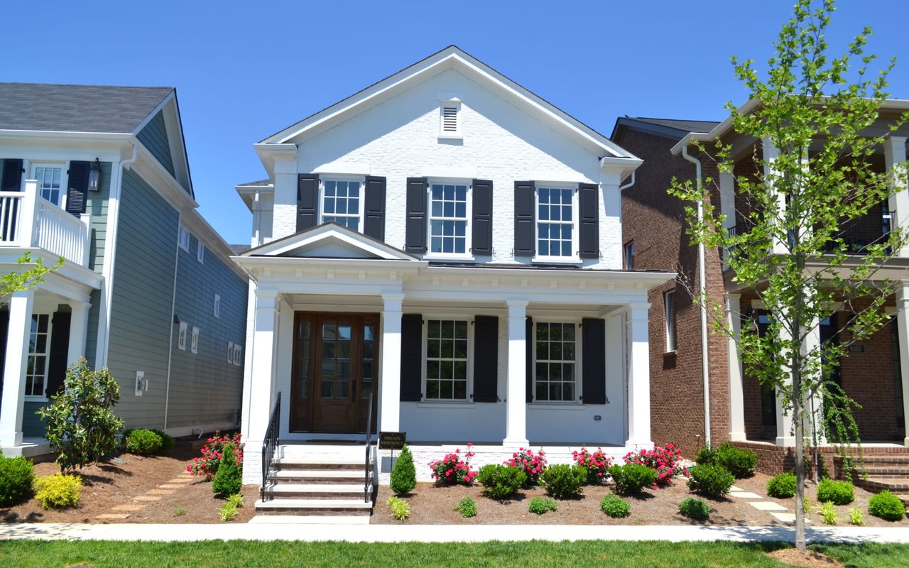 A two-story Colonial-style white house with a flower and plant box, a front porch with railings, a walkway, and a front lawn.