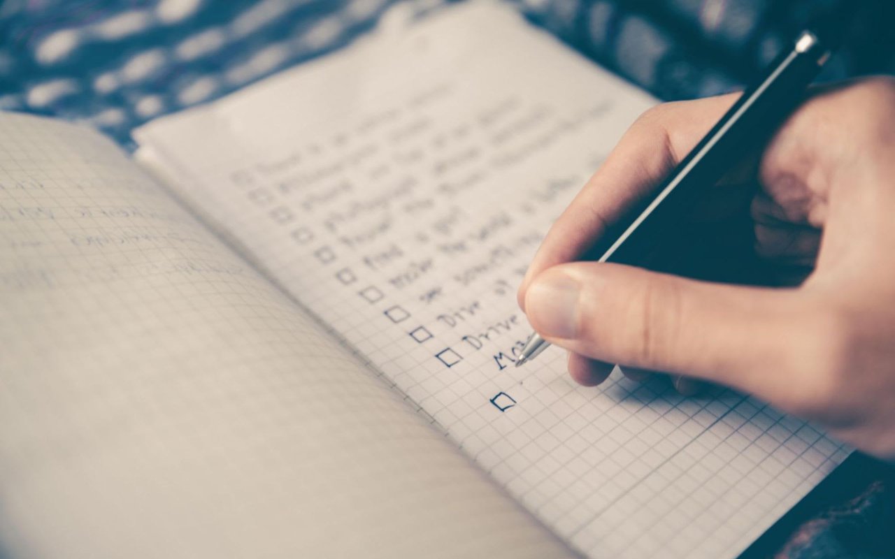 A photo of a hand holding a pen while writing a to-do list.