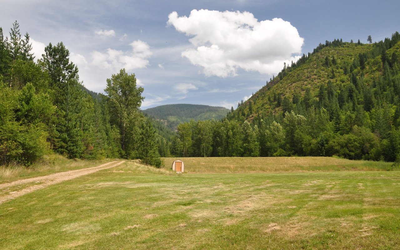 Tall, evergreen-covered mountains flank both sides of the valley, meeting in the background under a partly cloudy sky.