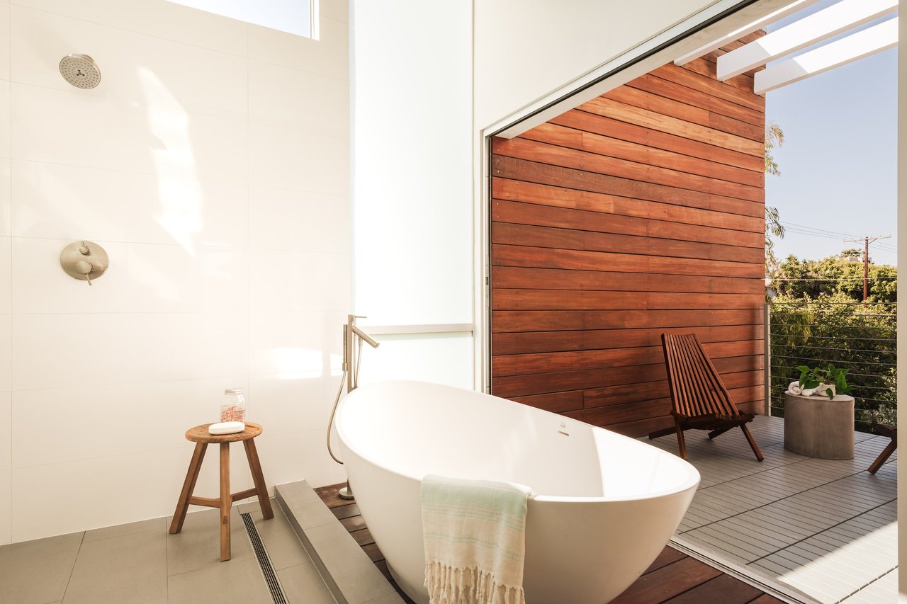  A spacious, bright bathroom features a modern white freestanding bathtub on a raised wooden platform.