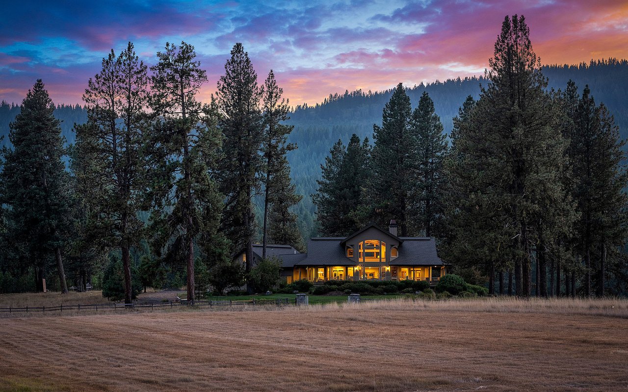  A charming house, possibly an Oregon mountain house, nestled in a clearing surrounded by tall evergreen trees.
