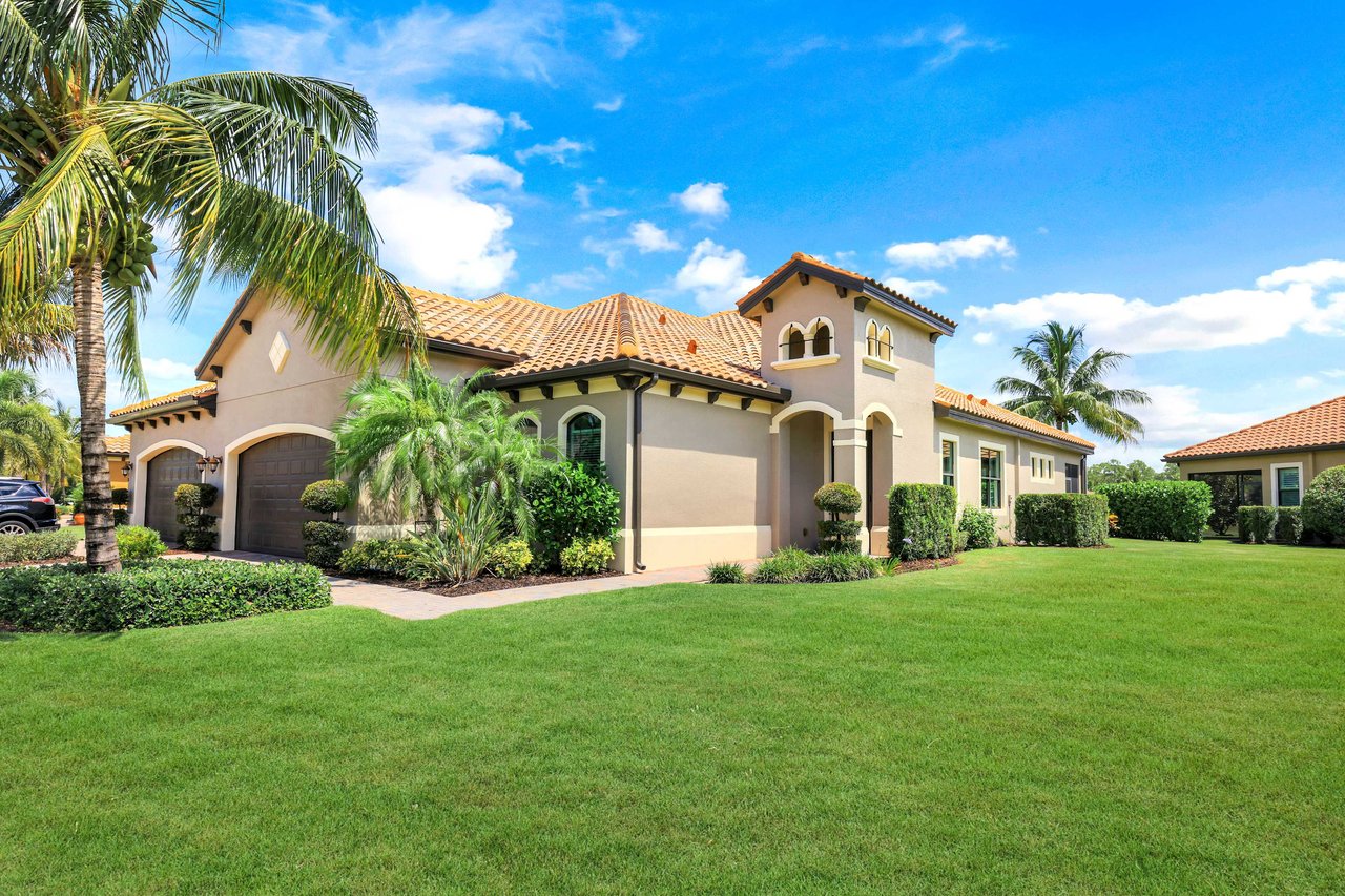  A Mediterranean-style house with a light brown stucco exterior and a terracotta tile roof stands under a bright blue sky with fluffy white clouds.