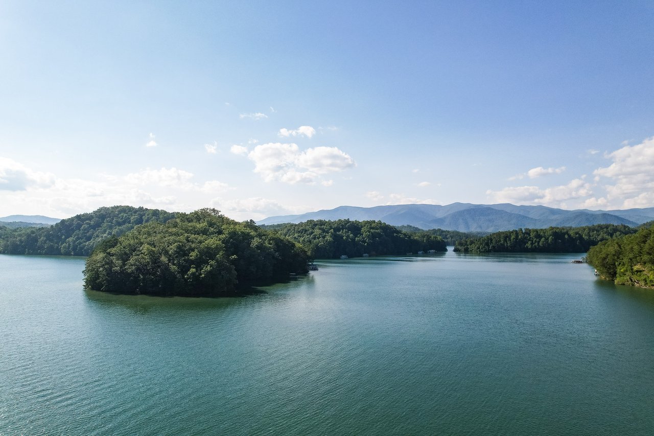 Alt= Serene lake with lush islands and hills under a clear sky, reflecting nature's beauty—an ideal scene for prime real estate