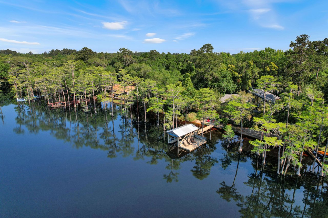 An aerial view of Lake Bradford.  The lake is surrounded by dense greenery and a few houses or cabins along the shoreline. The water is calm and reflective.