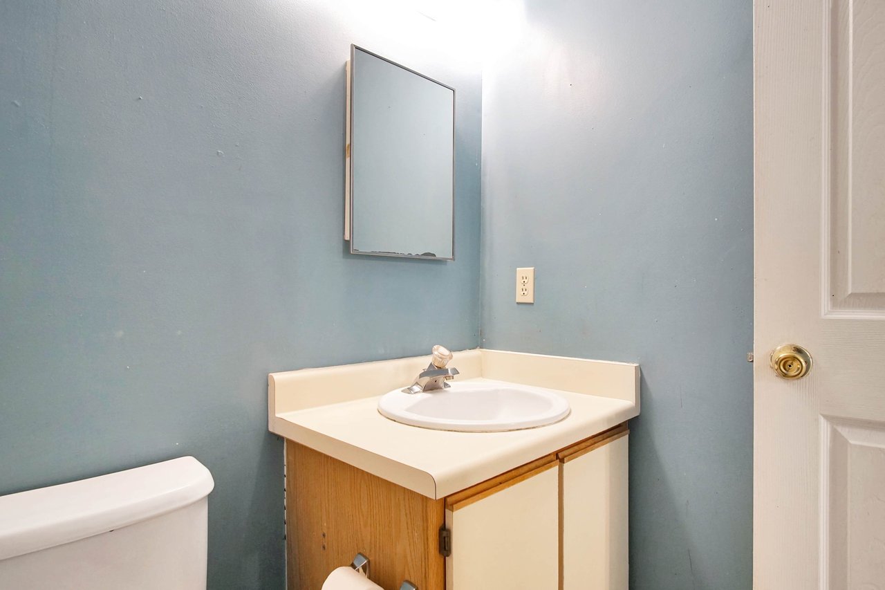 Photo of primary bathroom featuring lightly colored blue walls, a vanity light fixture, a medicine cabinet mirror, a vanity with white sink, light wood cabinets, and a toilet at 2709 Oak Park Court, Tallahassee, Florida 32308